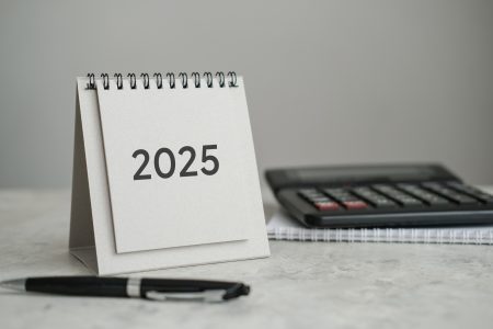 Desk calendar 2025, calculator and pen on the table